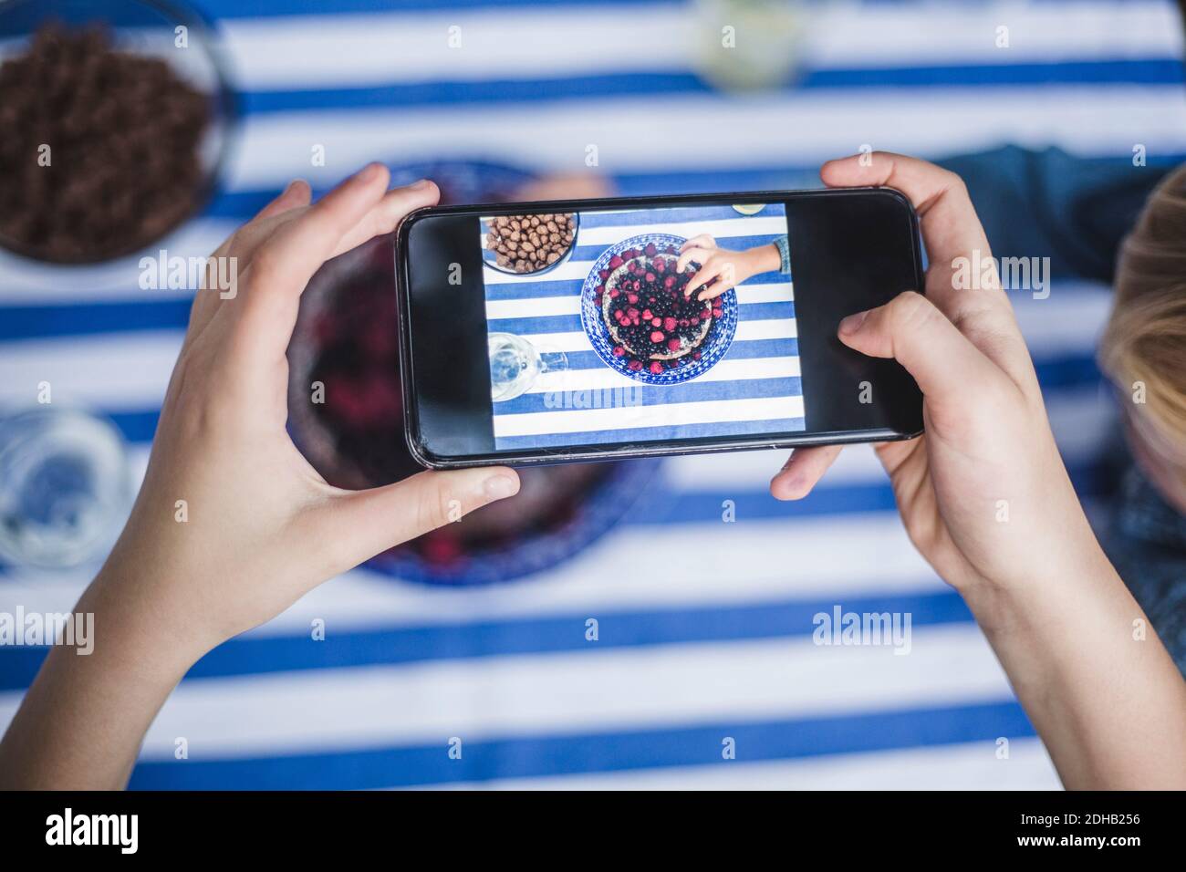 Main courte de fille avec smartphone photographiant garçon ayant dessert à table Banque D'Images