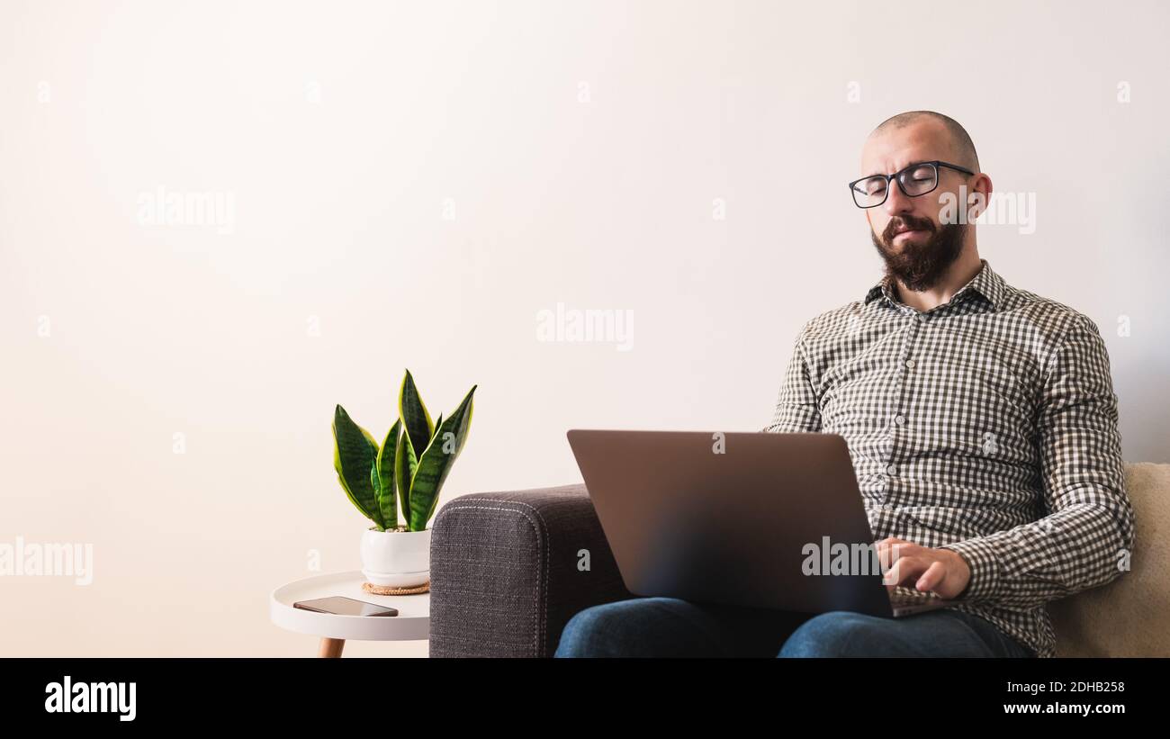 Jeune homme adulte travaille sur son ordinateur portable à la maison, intérieur minimaliste moderne Banque D'Images