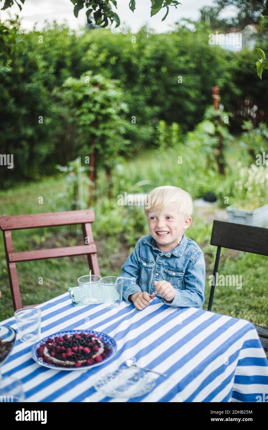 Un garçon souriant qui regarde loin tout en étant assis à la table à manger arrière-cour Banque D'Images