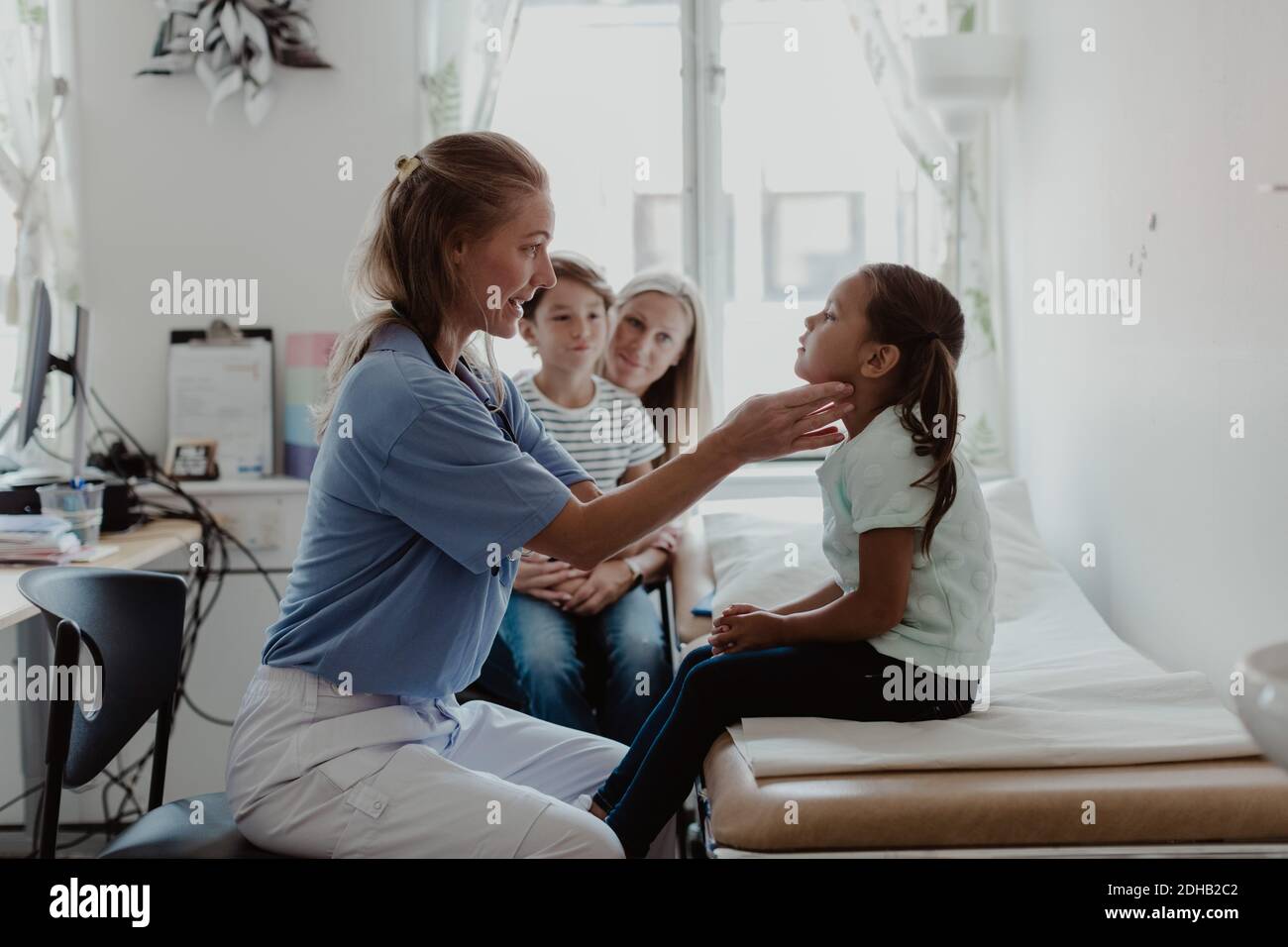 Femme médecin examinant la gorge de la fille pendant que la famille est assise salle médicale Banque D'Images