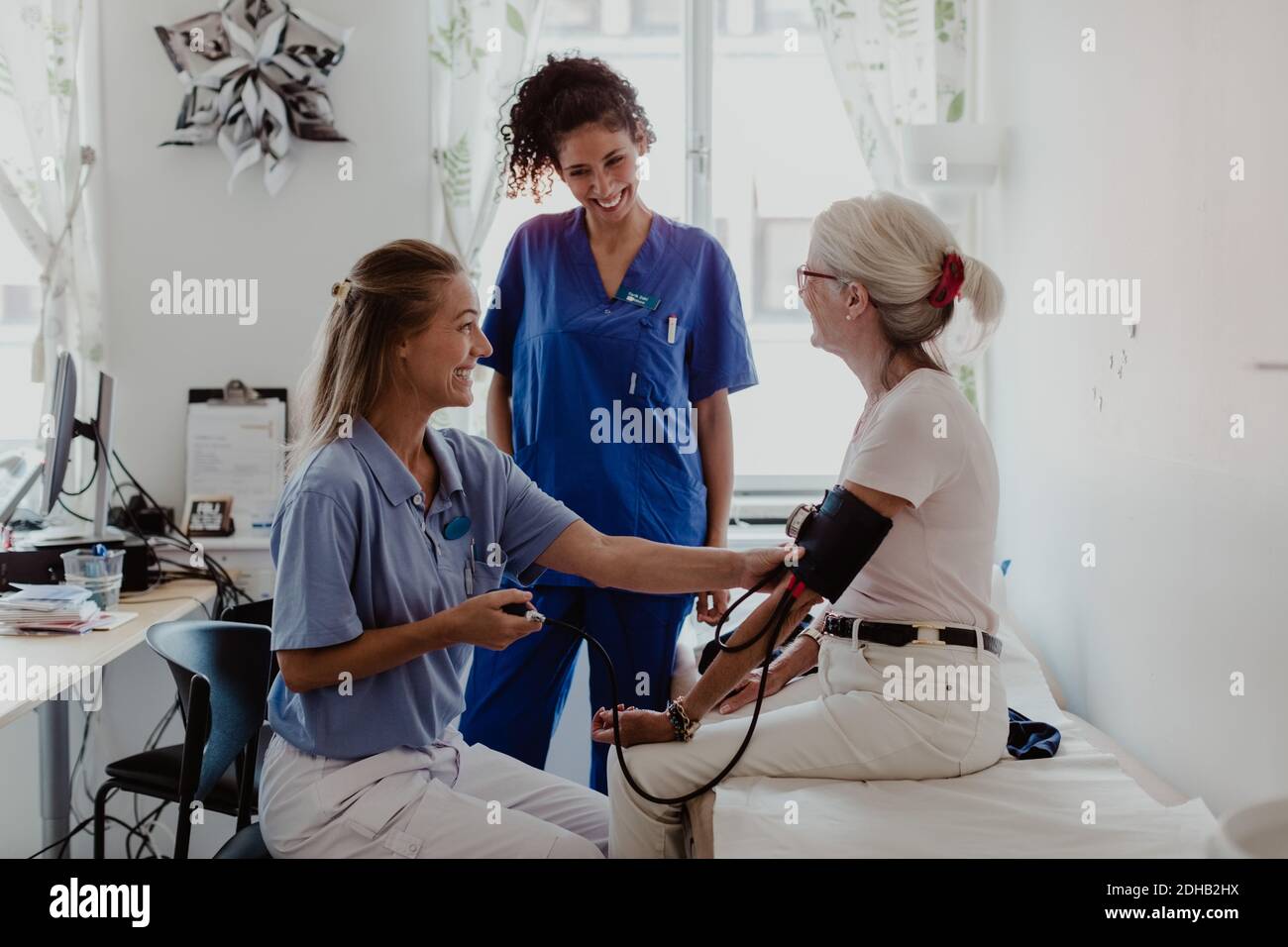 Médecin souriant vérifiant la pression artérielle du patient assis chambre d'hôpital Banque D'Images