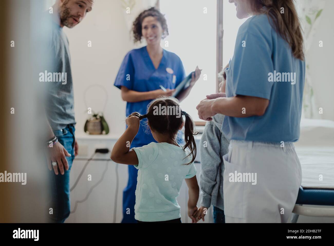 Le père parle avec les enfants tandis que les travailleurs de la santé les regardent dans la salle d'examen médical Banque D'Images