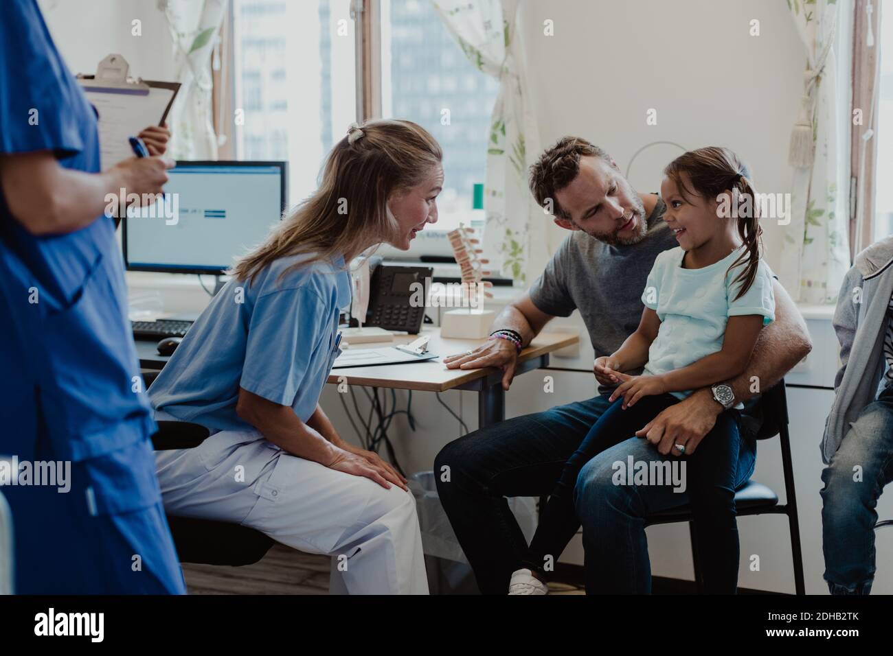 Pédiatre féminin parlant à une fille souriante assise avec son père salle d'examen médical Banque D'Images