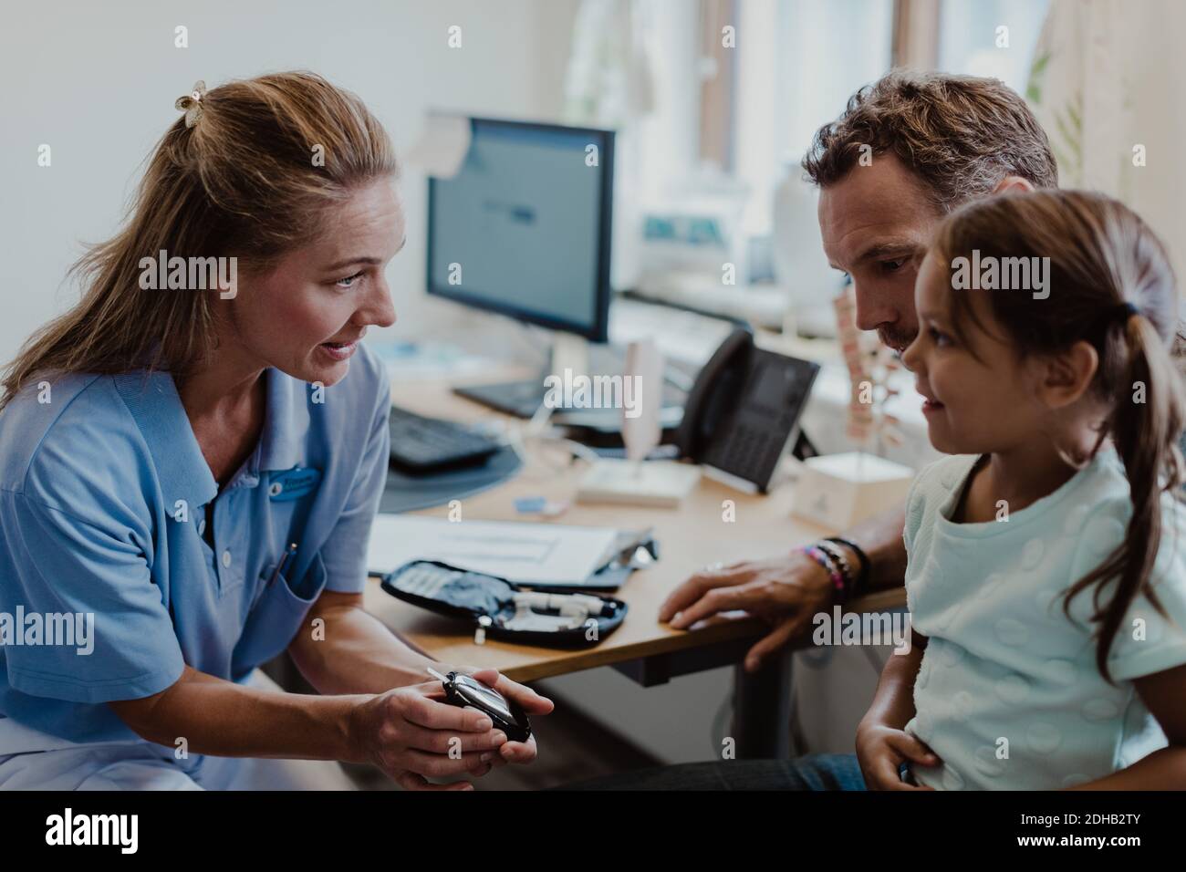 Fille souriante regardant un médecin montrant un glaucomètre en examen médical chambre Banque D'Images