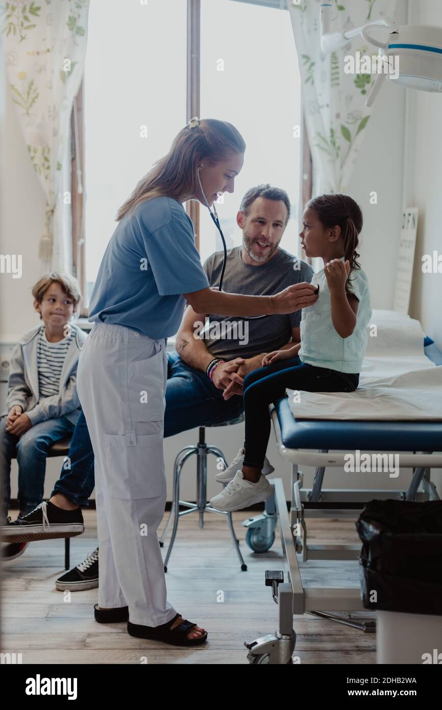 Pédiatre vérifiant fille avec stéthoscope tout en étant assis avec la famille dedans salle d'examen médical Banque D'Images