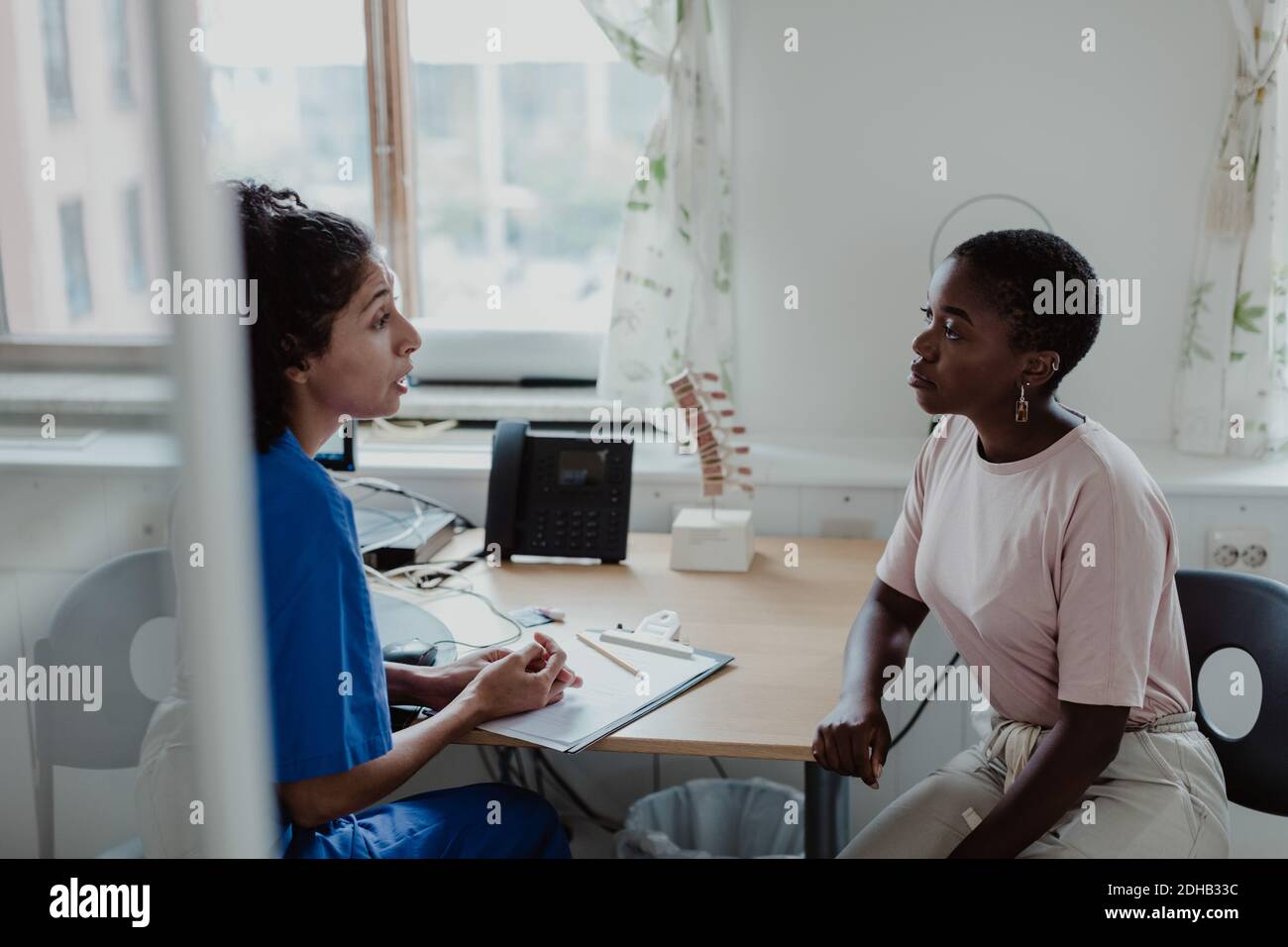 Une employée de soins de santé expliquant les dossiers médicaux aux jeunes patients dans bureau Banque D'Images