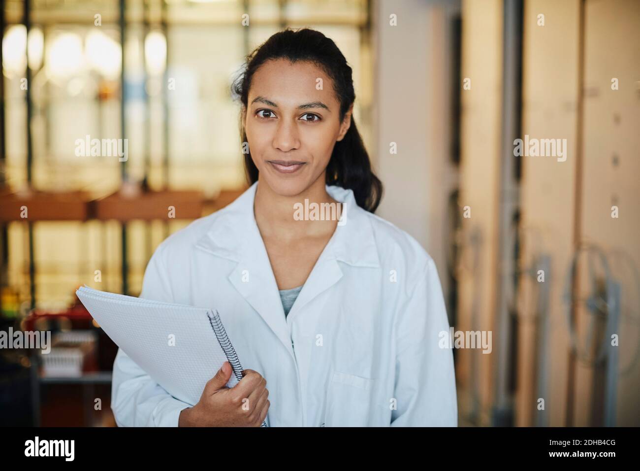 Portrait d'un jeune étudiant en chimie confiant portant un manteau de laboratoire debout avec livre à l'université Banque D'Images