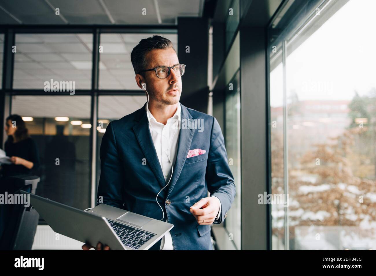 Entrepreneur attentif tenant un ordinateur portable tout en regardant par la fenêtre dans le bureau Banque D'Images