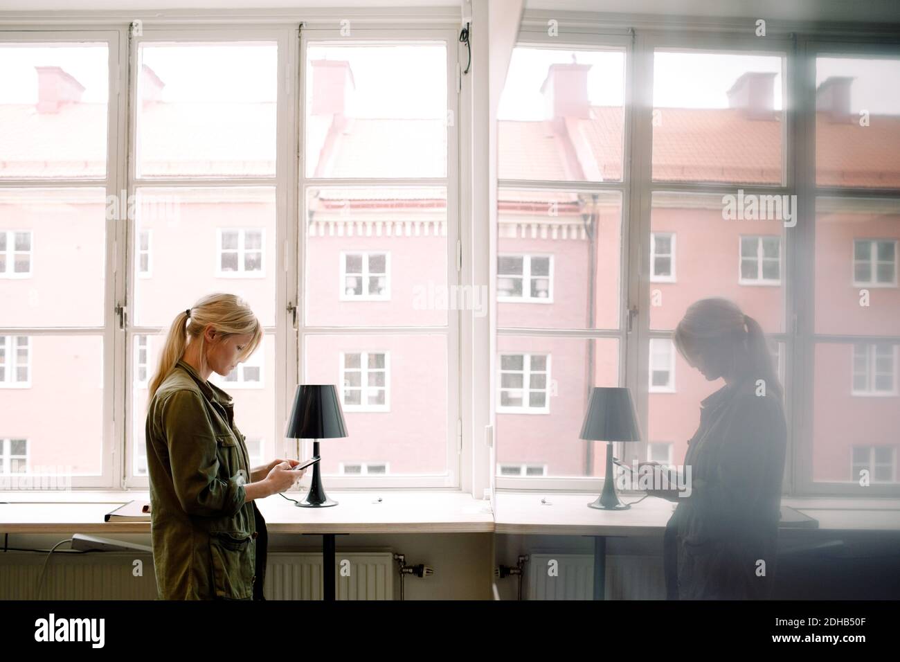 Femme d'affaires utilisant un smartphone tout en réfléchissant sur le verre au bureau Banque D'Images