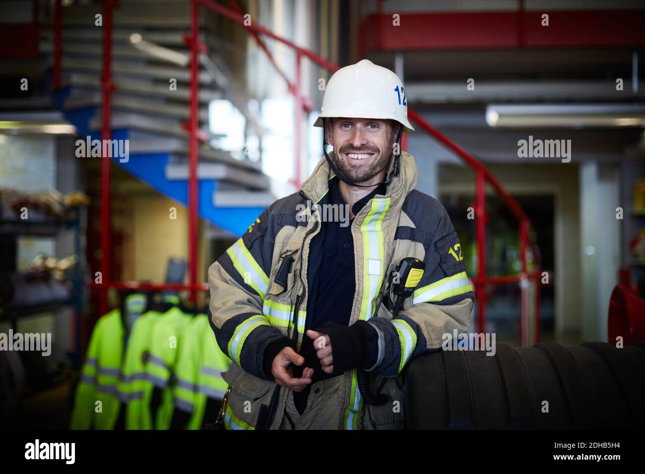 Portrait d'un pompier souriant portant un costume de protection à la caserne de pompiers Banque D'Images