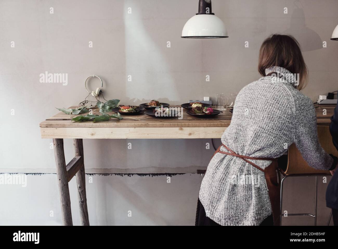 Vue arrière d'une femme entrepreneur debout près d'une table avec de la nourriture plaques contre le mur à l'atelier Banque D'Images