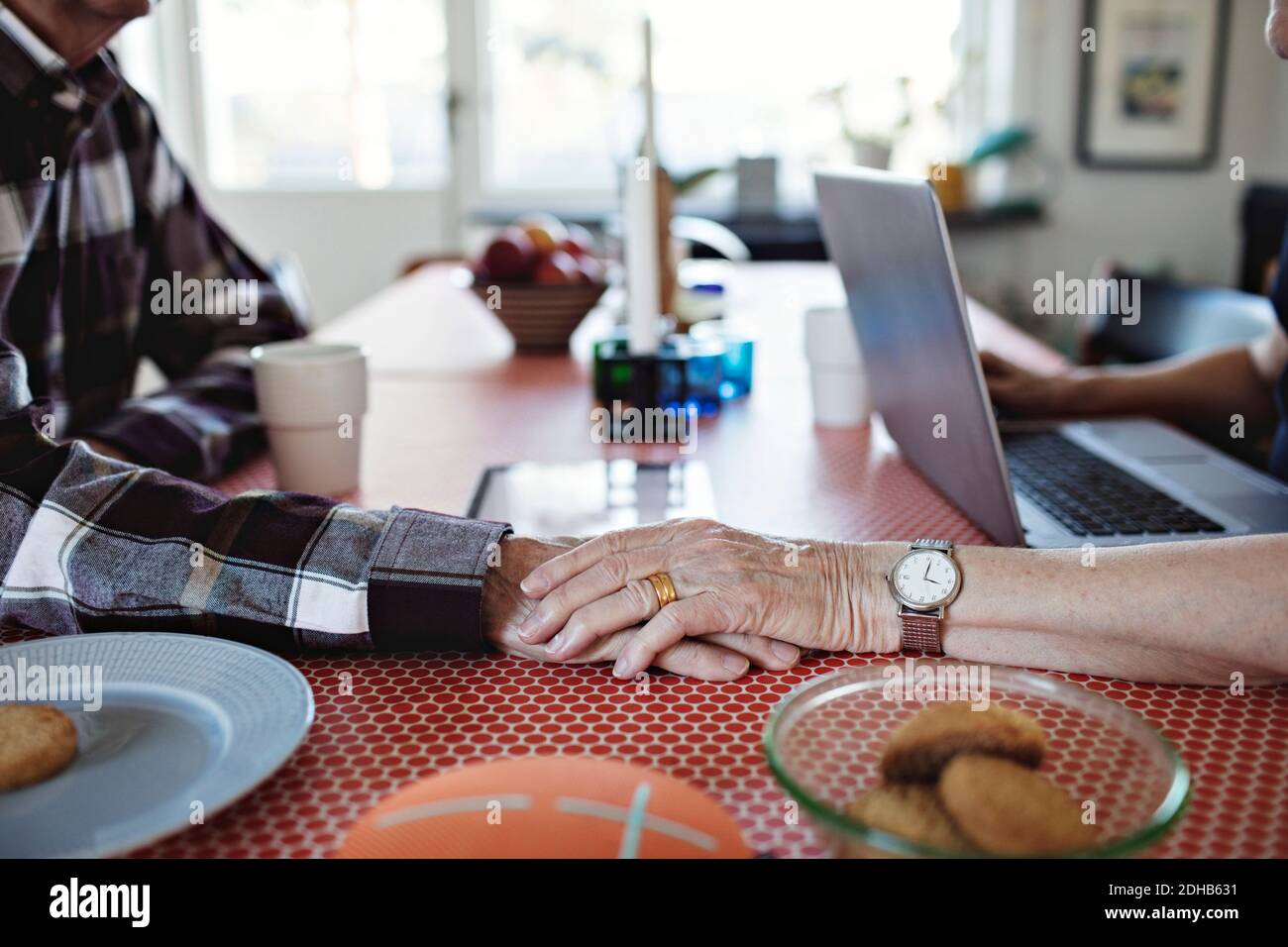Image rognée d'une femme âgée tenant les mains avec l'homme table à manger à la maison Banque D'Images