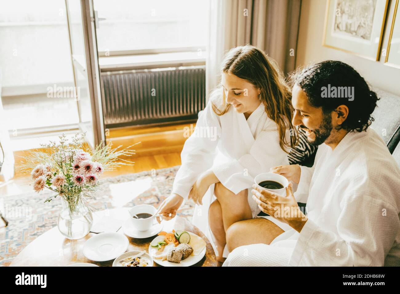 Vue en grand angle de couple dans des peignoirs en prenant le petit déjeuner à chambre d'hôtel Banque D'Images