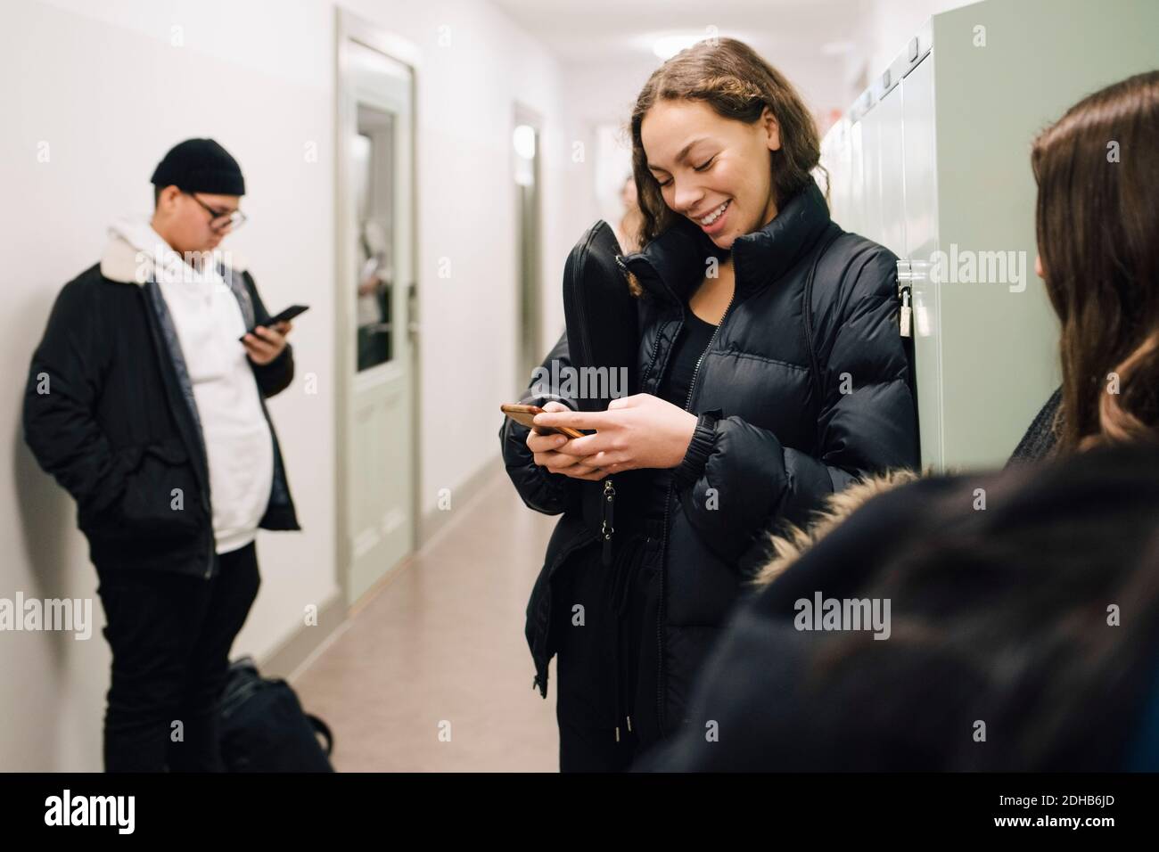 Adolescent souriant étudiant utilisant un smartphone dans le couloir Banque D'Images