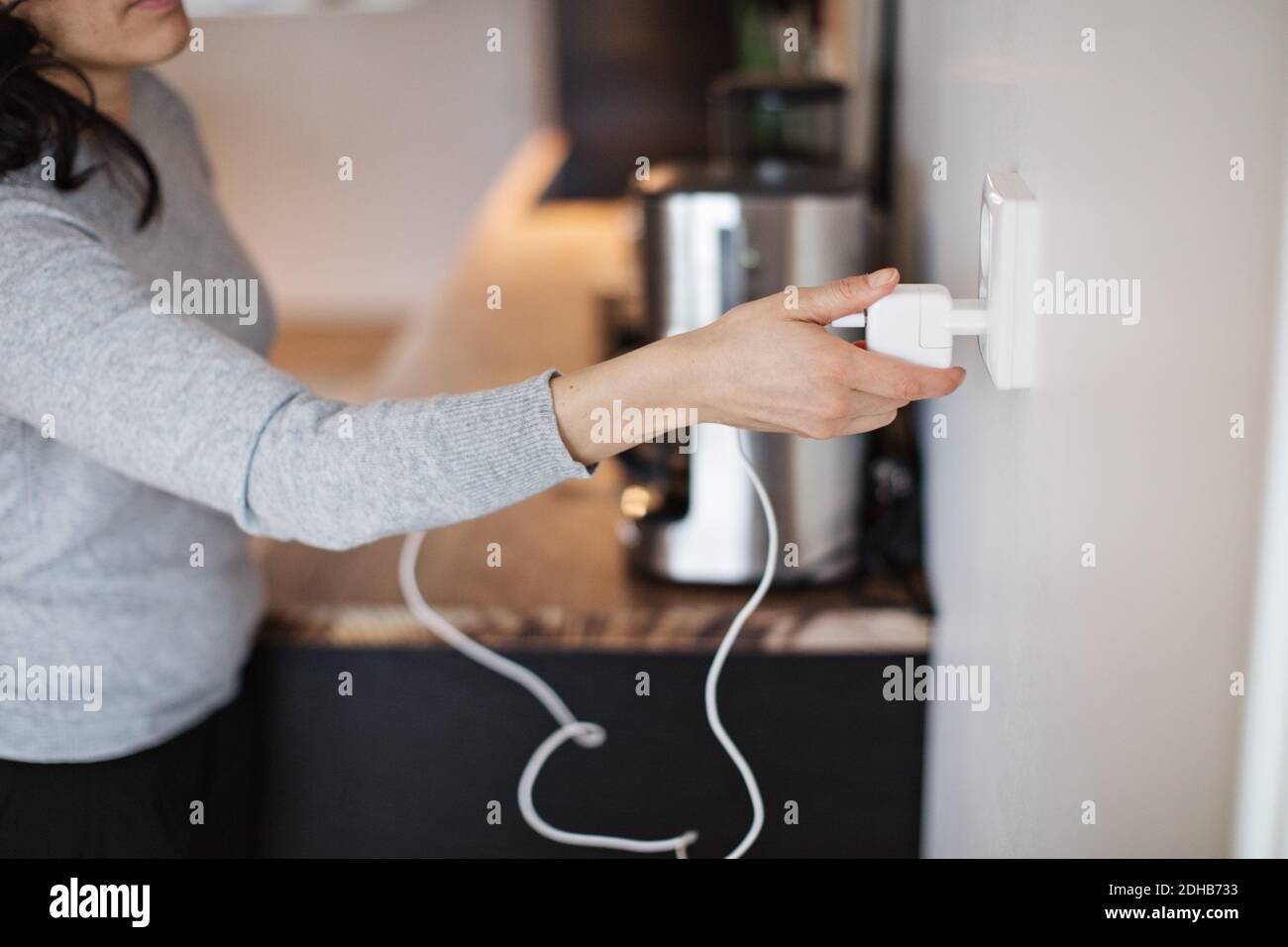 Section médiane de la femme qui branche le chargeur de téléphone portable au mur accueil Banque D'Images