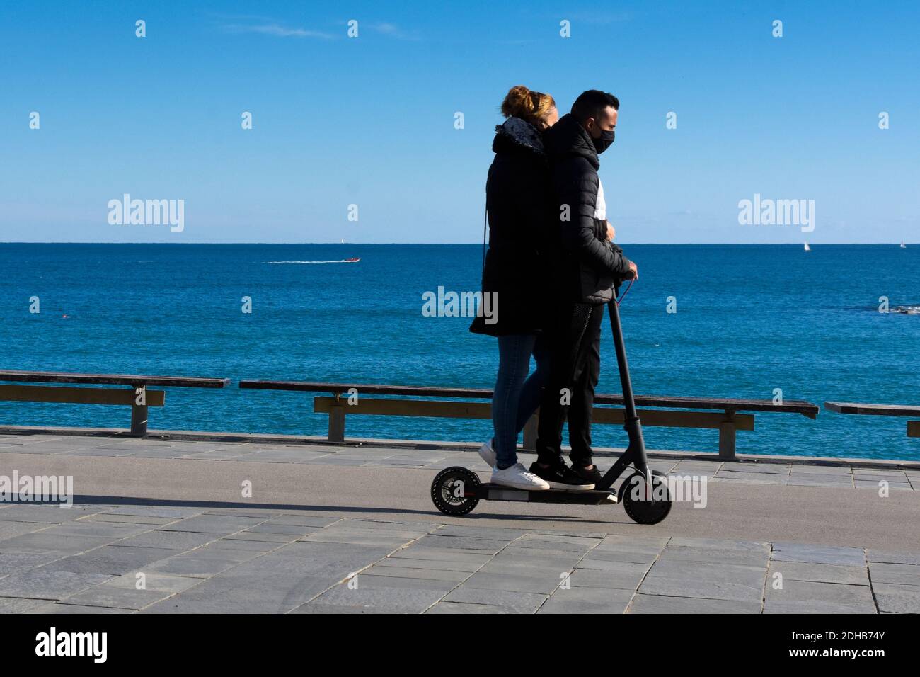Un jeune couple monte sur le même scooter électrique le long de la promenade. Banque D'Images
