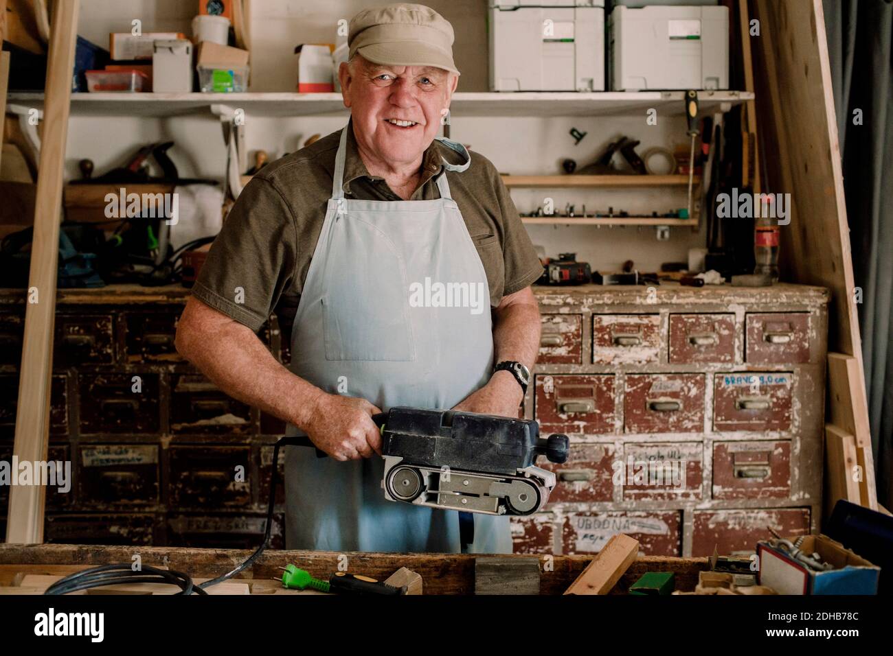 Portrait d'un homme âgé souriant et confiant tenant un outil électrique à l'atelier Banque D'Images