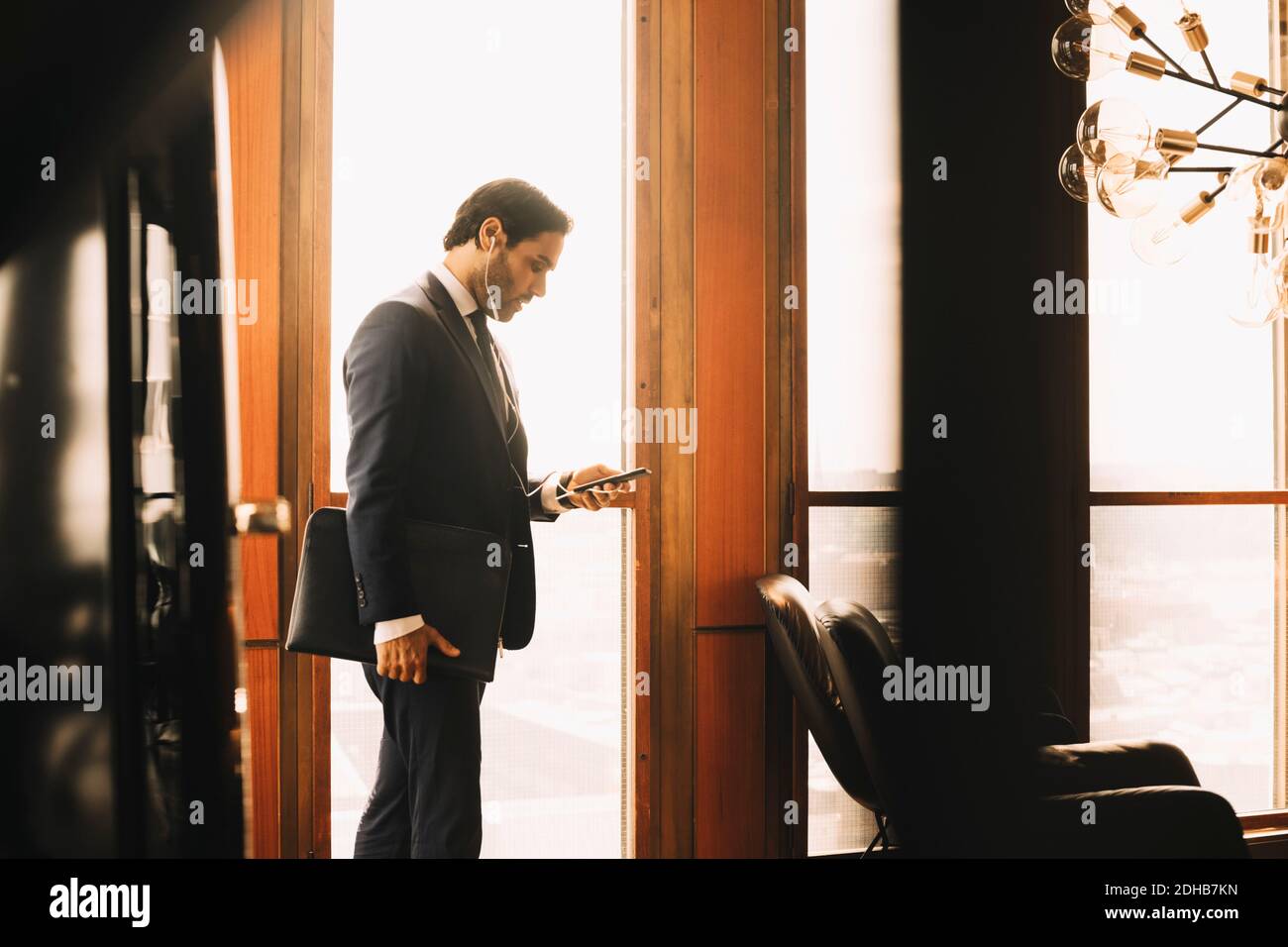 Vue latérale d'un conseiller financier masculin portant un casque pendant l'utilisation smartphone par fenêtre au bureau juridique Banque D'Images