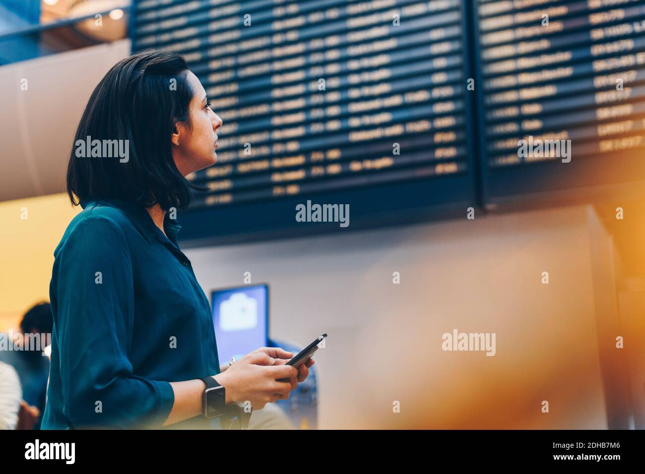 Vue latérale d'une femme d'affaires de taille moyenne qui regarde le départ de l'arrivée montez à l'aéroport Banque D'Images
