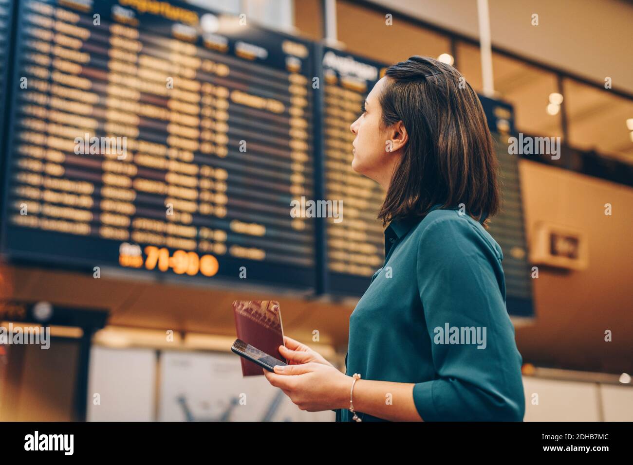 Vue latérale d'une femme d'affaires regardant le panneau de départ à l'arrivée aéroport Banque D'Images