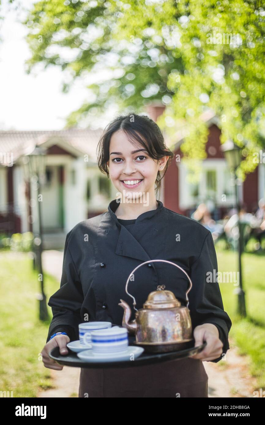 Portrait d'une serveuse jeune femme confiante souriant tout en tenant le service plateau contre le restaurant Banque D'Images Portrait d'une serveuse jeune femme confiante souriant tout en tenant le service plateau contre le restaurant Banque D'Images