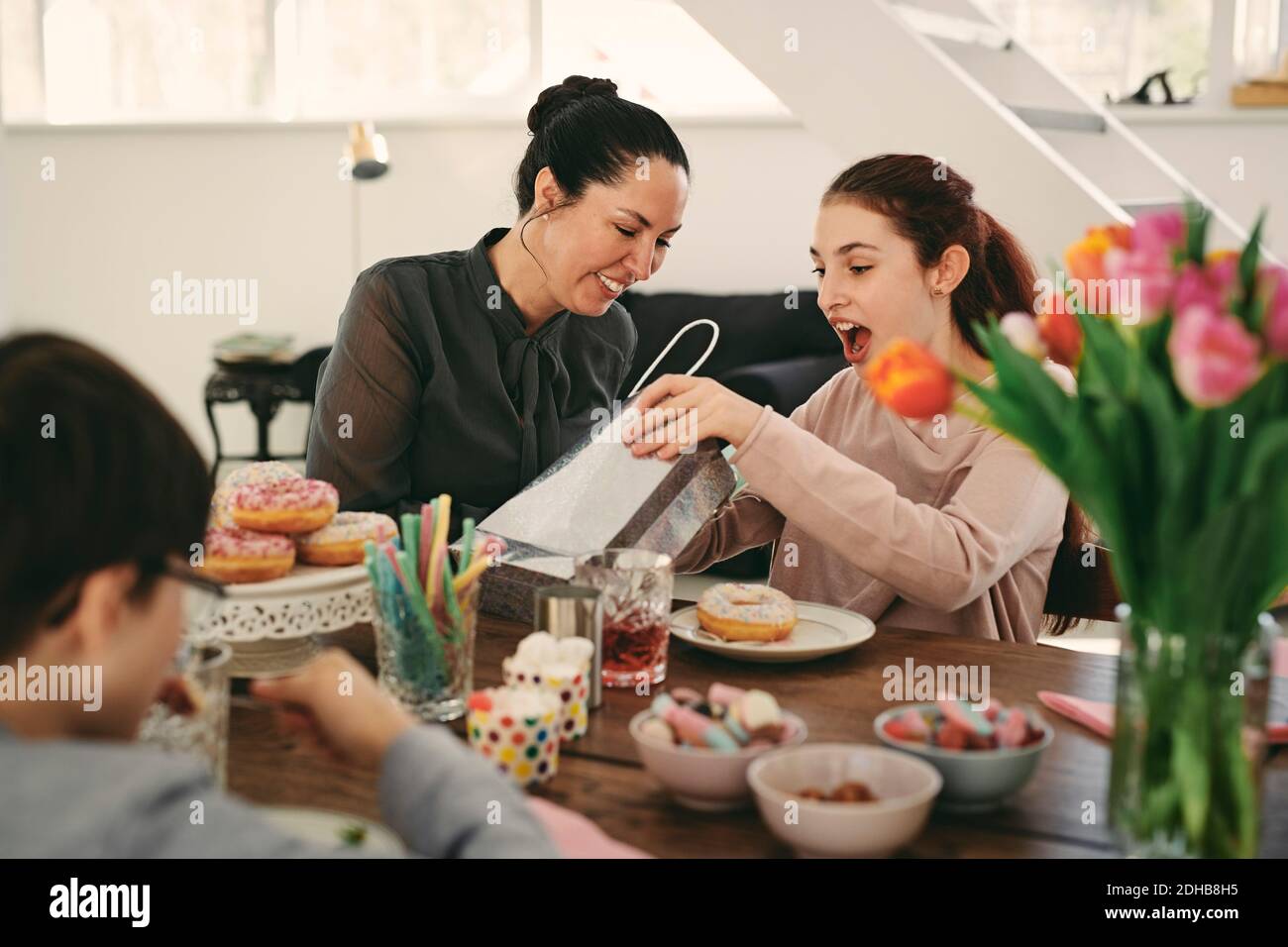 Fille surprise regardant le sac tout en étant assise avec la mère pendant repas en fête d'anniversaire Banque D'Images