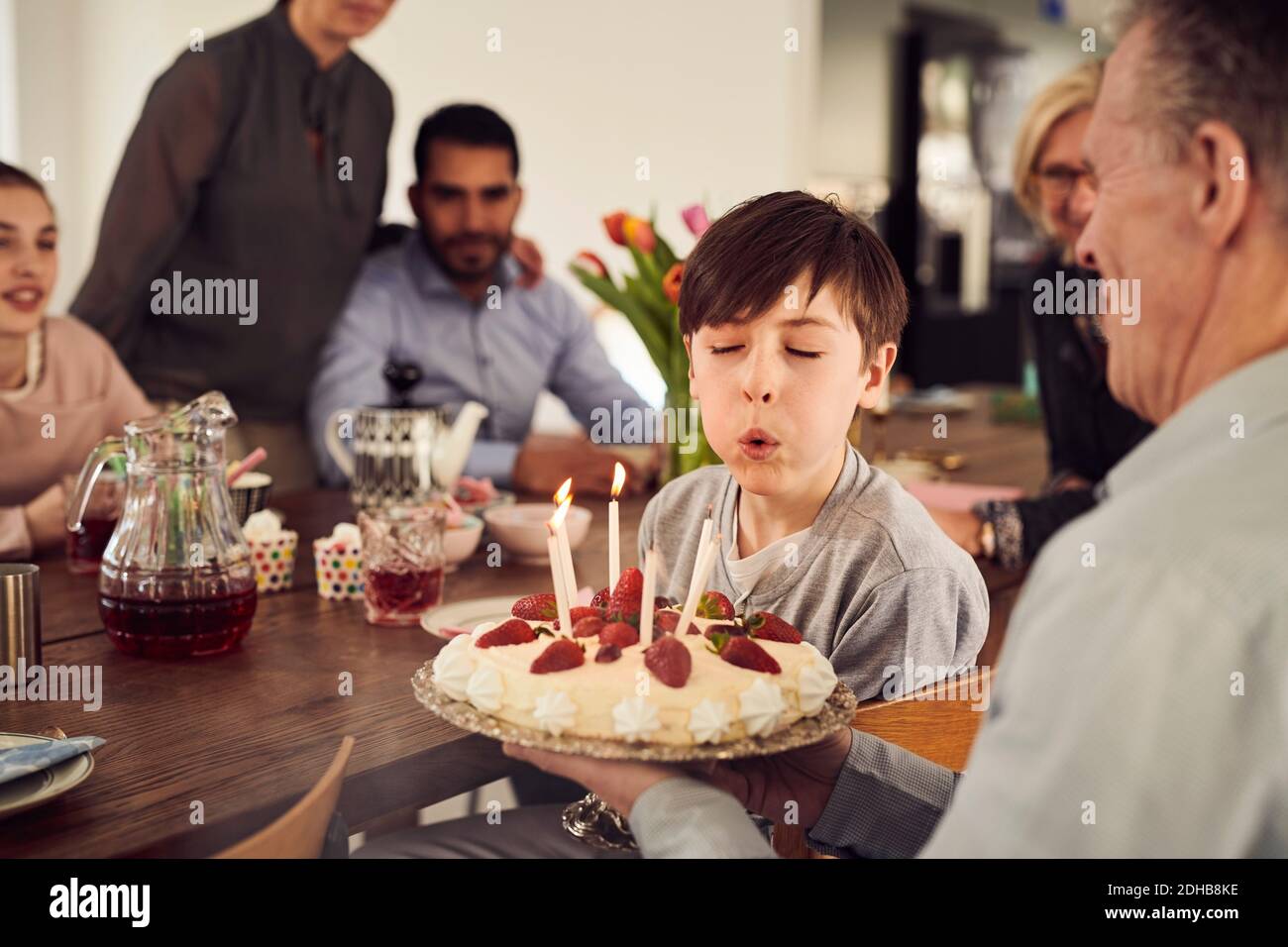 Garçon soufflant des bougies sur le gâteau d'anniversaire tout en appréciant dans la fête avec la famille à la maison Banque D'Images
