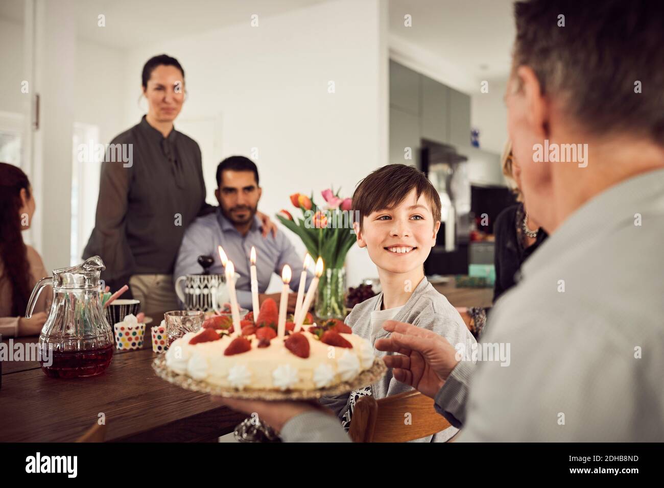 Garçon souriant regardant le grand-père tenant le gâteau d'anniversaire avec la famille en fête Banque D'Images