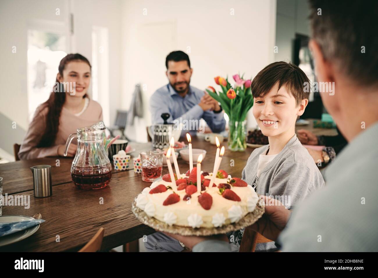 Garçon regardant le gâteau d'anniversaire tout en étant assis avec la famille à accueil Banque D'Images