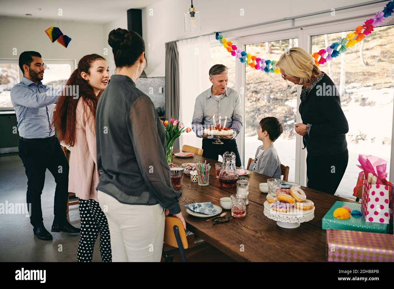 Grand-père montrant gâteau d'anniversaire à garçon tout en appréciant la famille heureuse à la fête Banque D'Images