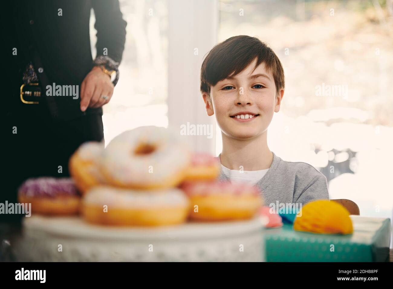 Portrait d'un garçon souriant assis par la grand-mère à la table de salle à manger avec beignes au premier plan Banque D'Images