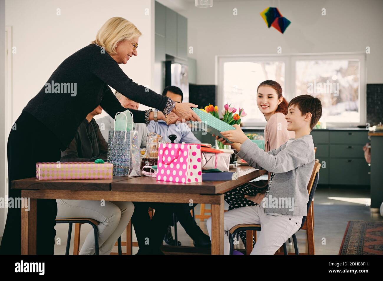 Grand-mère offrant un cadeau à un garçon assis avec sa famille au dîner tableau Banque D'Images