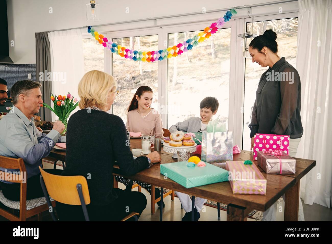 Famille regardant le garçon avec boîte cadeau tout en appréciant le repas à table pendant la fête d'anniversaire Banque D'Images