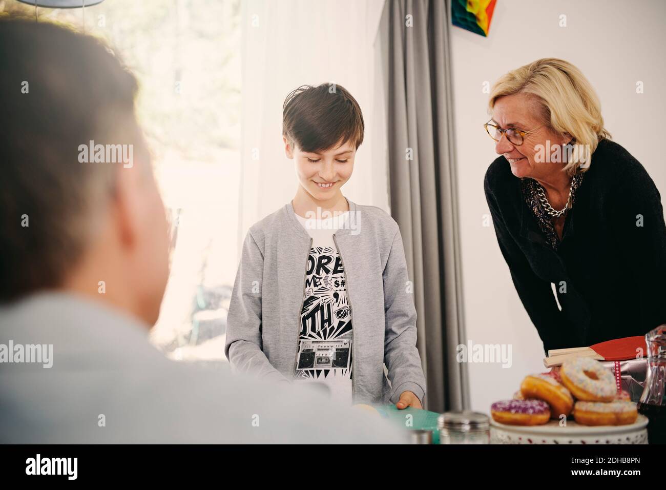 Garçon souriant regardant le cadeau d'anniversaire tout en se tenant debout avec la grand-mère à la table Banque D'Images