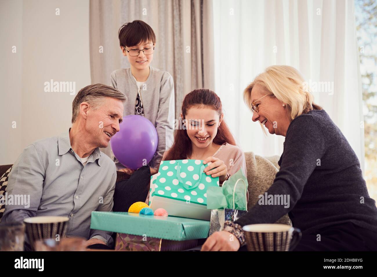 Famille regardant la fille souriante ouvrant des cadeaux sur le canapé à accueil Banque D'Images