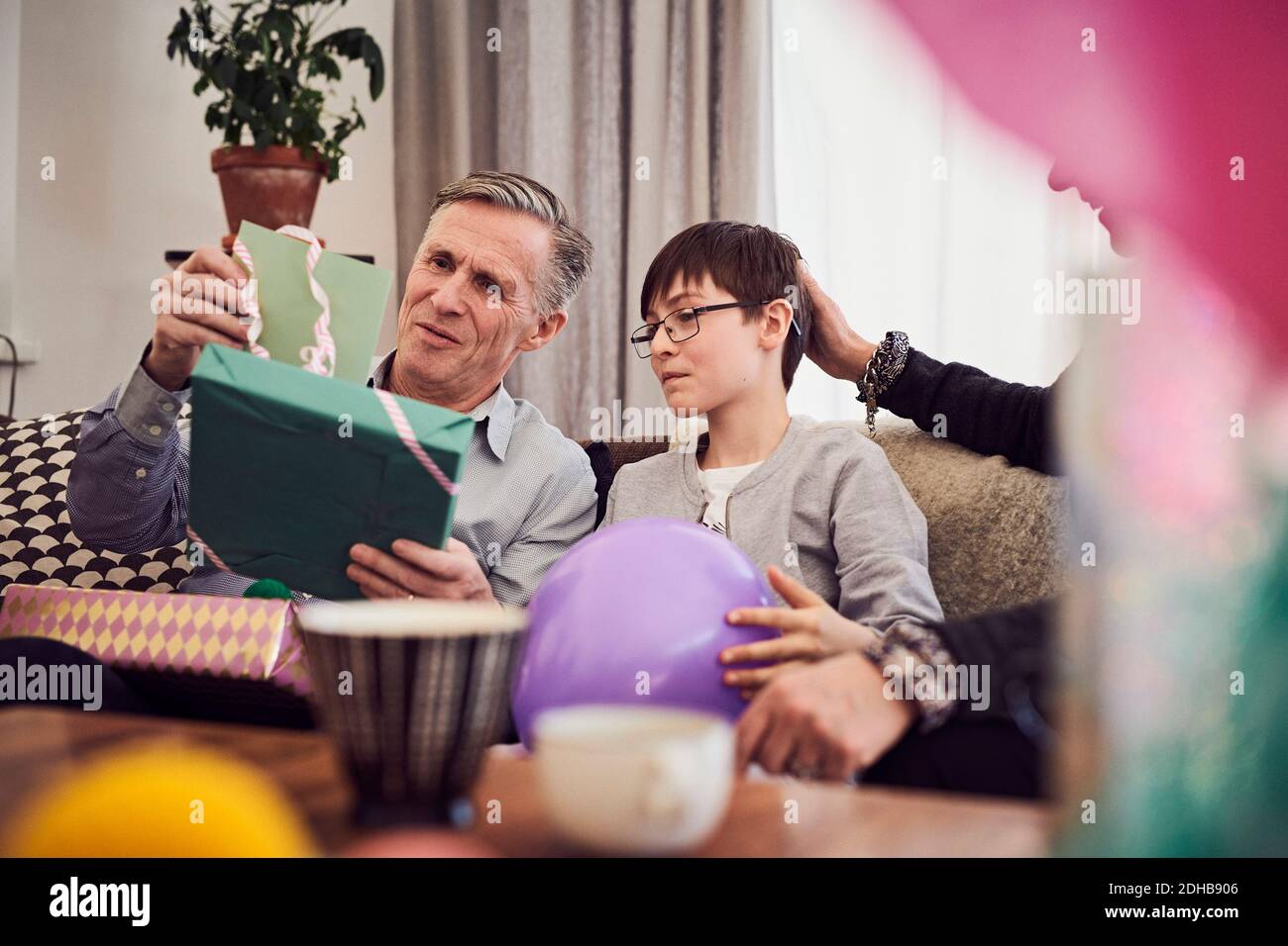 Garçon et grand-père regardant la carte de voeux et le cadeau d'anniversaire tout en étant assis sur un canapé Banque D'Images