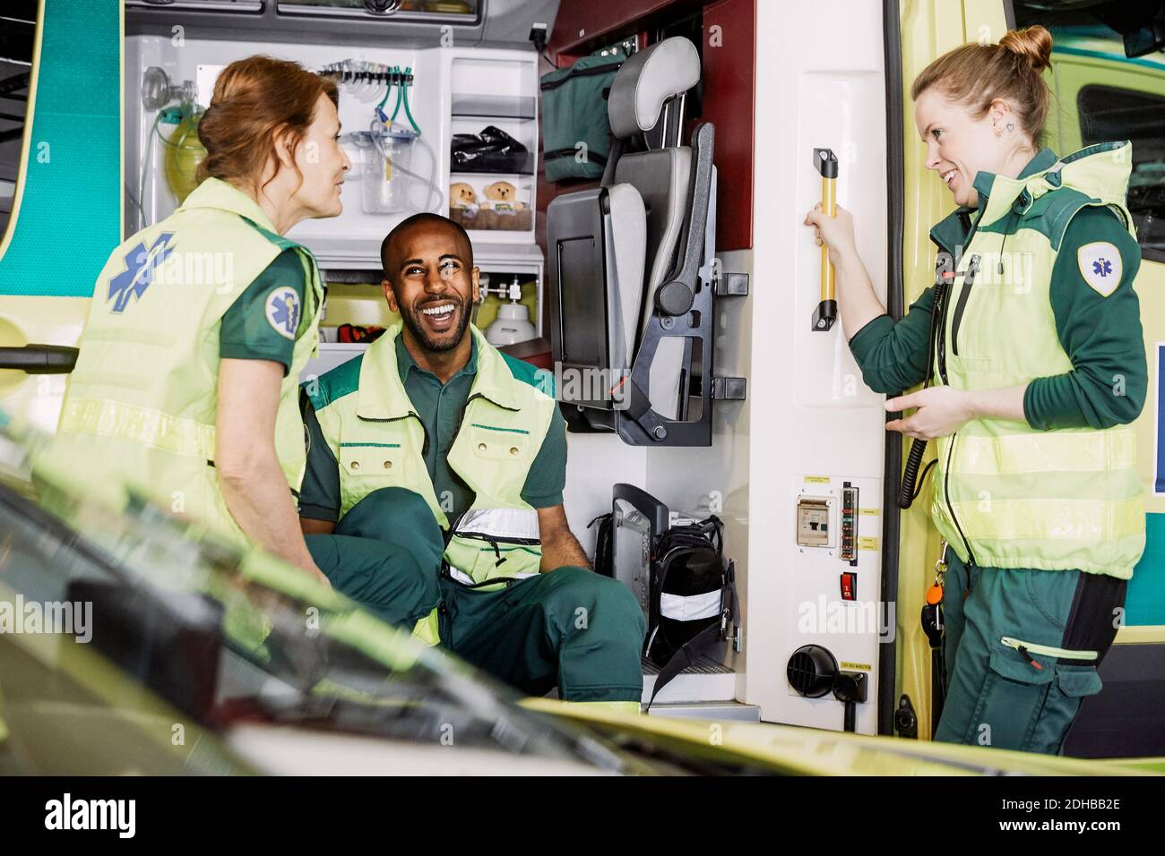 Heureux ambulanciers paramédicaux multi-ethniques parlant tout en étant assis dans une ambulance au parking lot Banque D'Images