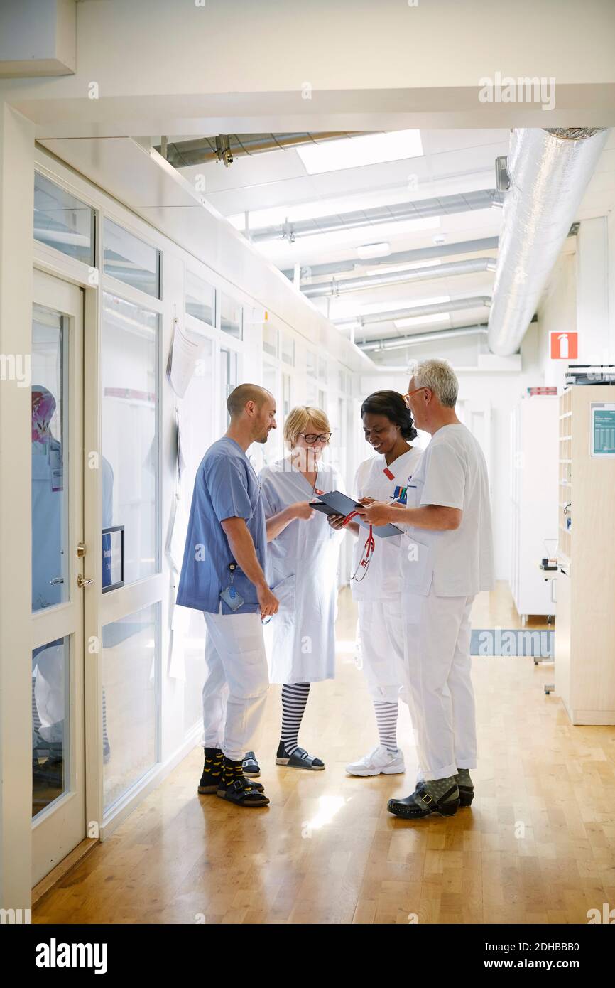 Toute la longueur des professionnels de la santé discutant sur tablette numérique pendant debout dans le couloir de l'hôpital Banque D'Images