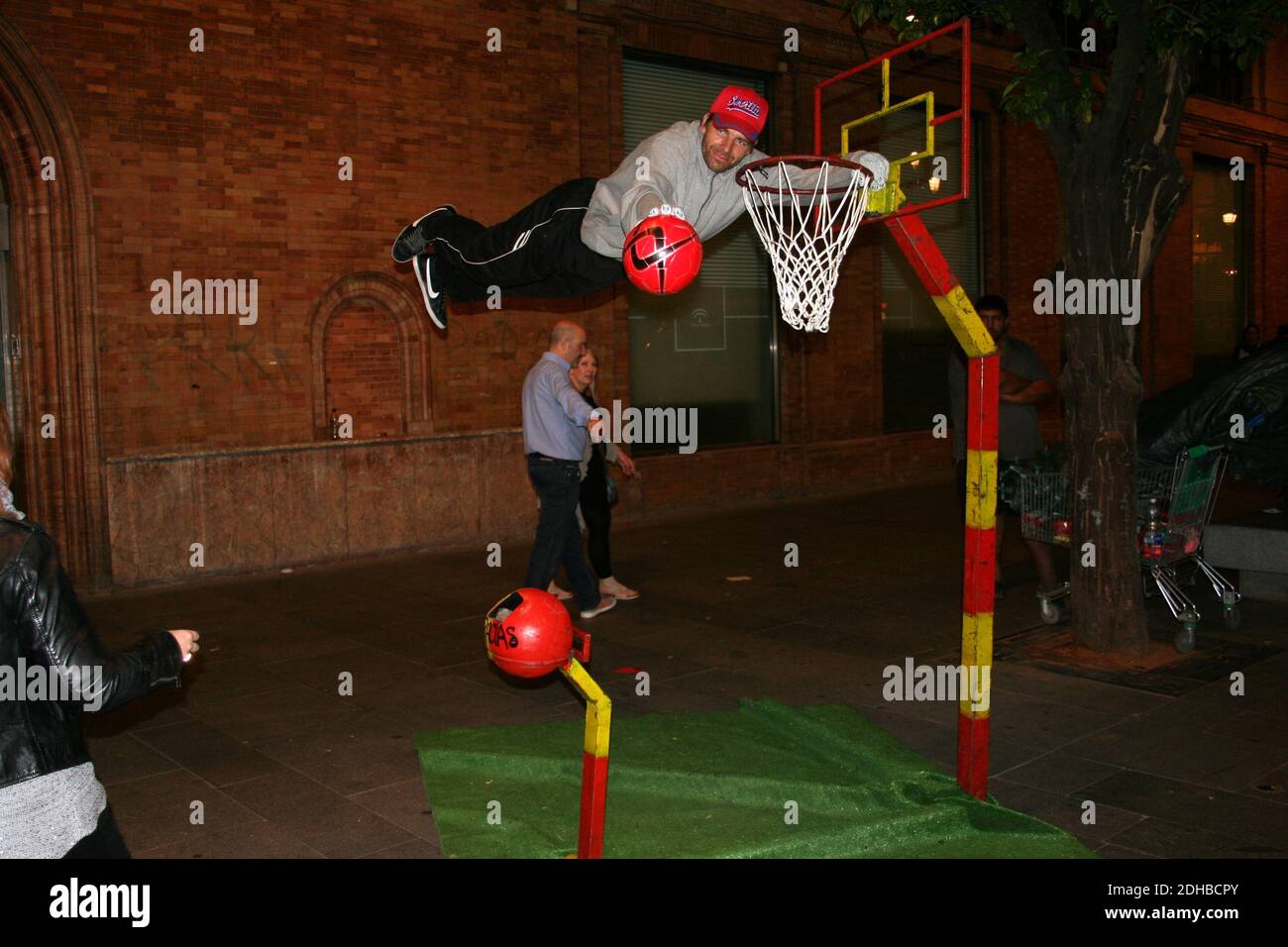 Un artiste de rue suspendu horizontalement en permanence à côté d'un filet de basket-ball Lors d'une chaude nuit d'été à Séville Espagne Banque D'Images