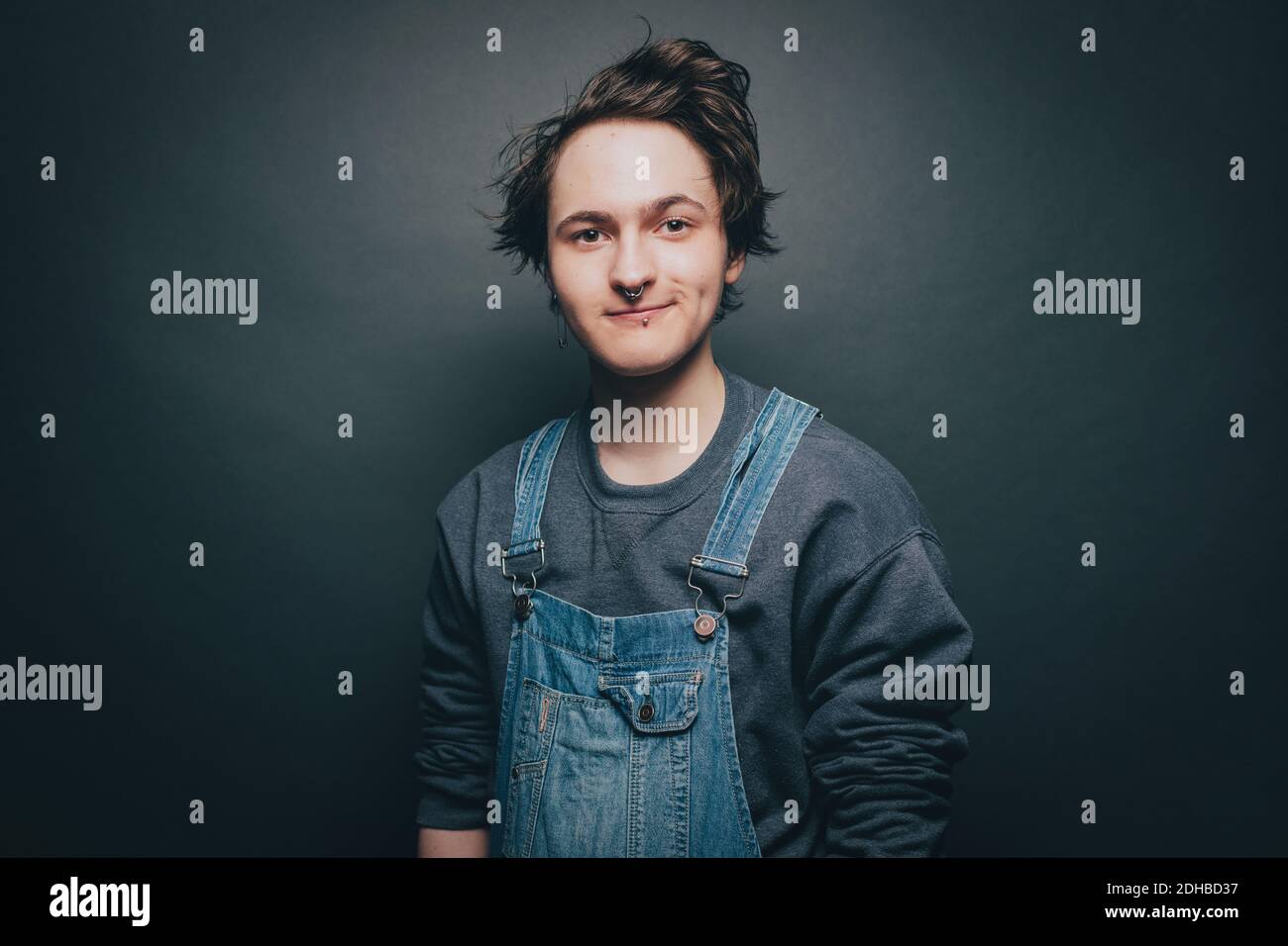 Portrait d'un jeune homme souriant portant une combinaison en denim sur fond gris arrière-plan Banque D'Images