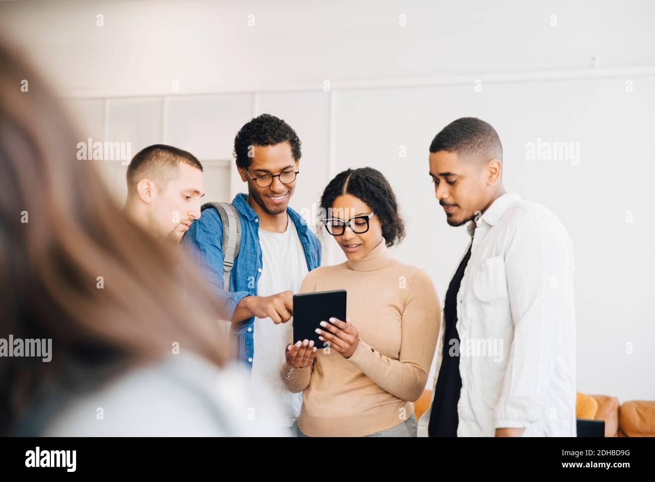 Un pirate informatique féminin montrant une tablette numérique à des collègues de sexe masculin se tenir contre le mur dans le bureau Banque D'Images