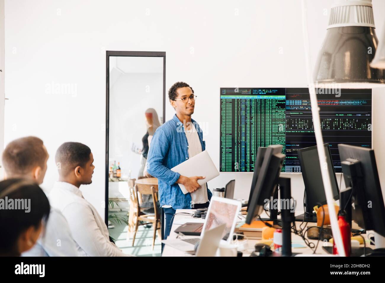 Hacker d'ordinateur expliquant le code sur l'écran de télévision aux programmeurs pendant réunion dans un bureau créatif Banque D'Images