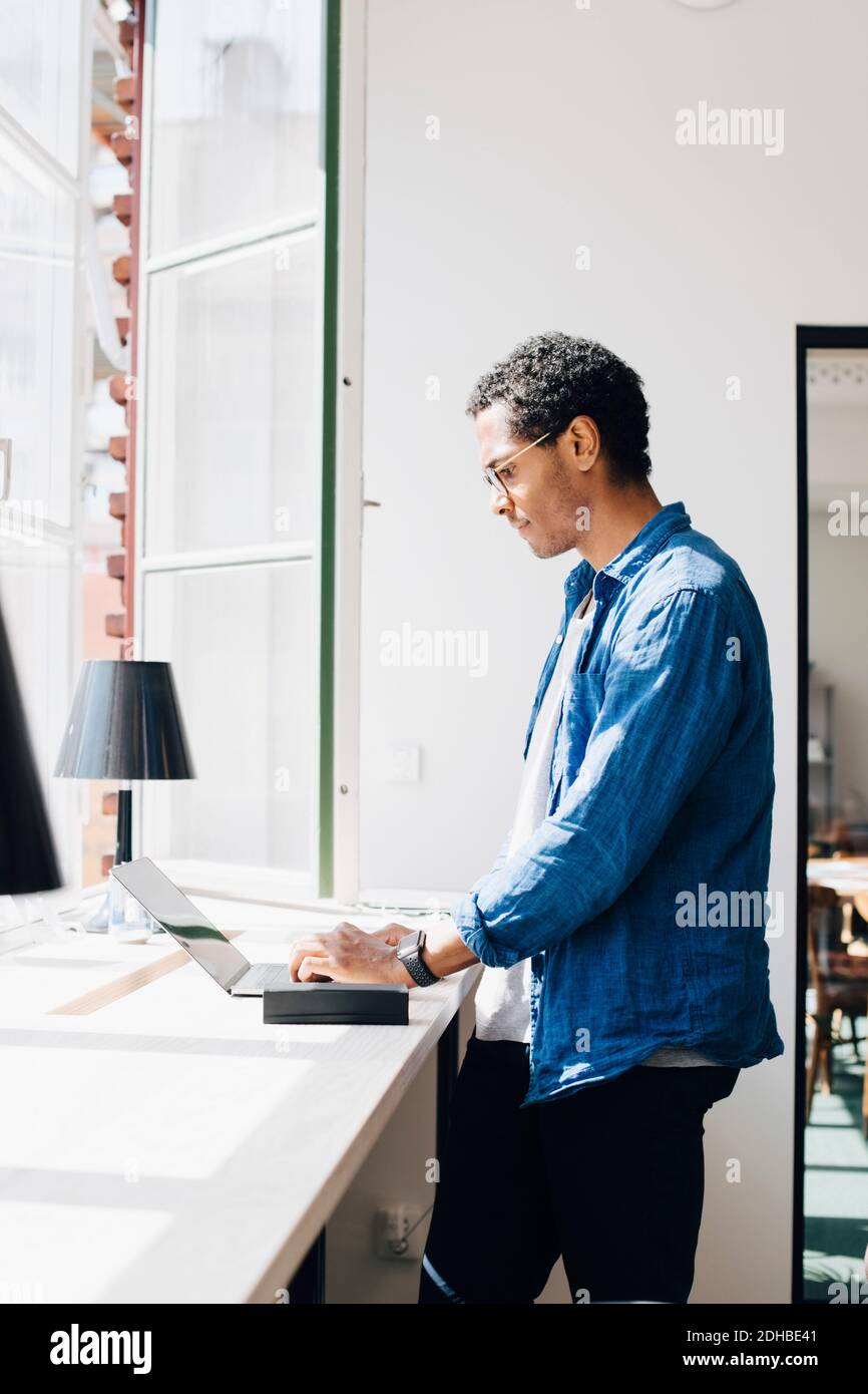 Vue latérale du pirate informatique travaillant sur un ordinateur portable au bureau par fenêtre dans le bureau Banque D'Images