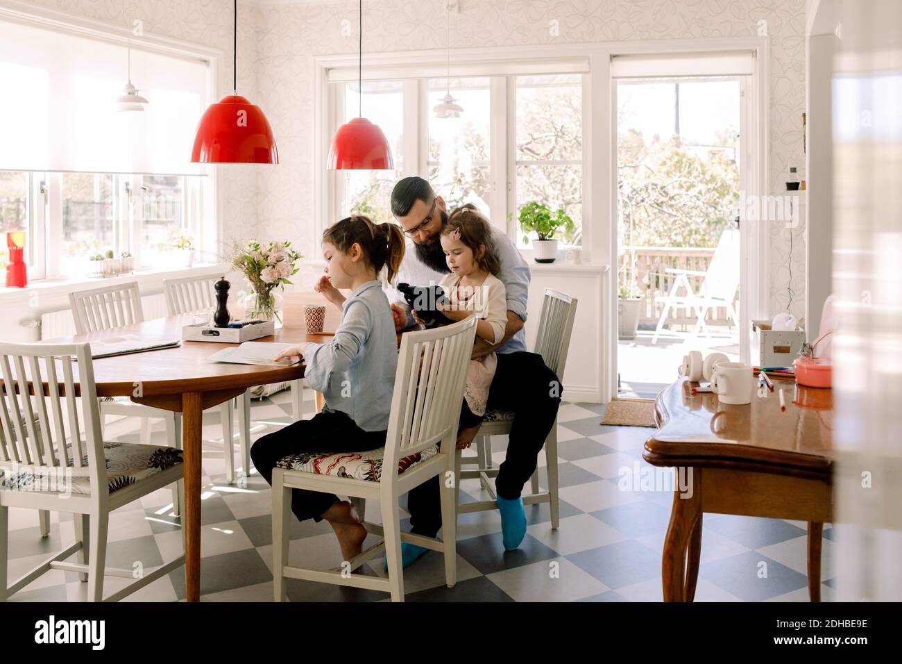 Père regardant une fille en utilisant une tablette numérique tout en étant assis avec fille qui fait ses devoirs à la table du dîner Banque D'Images