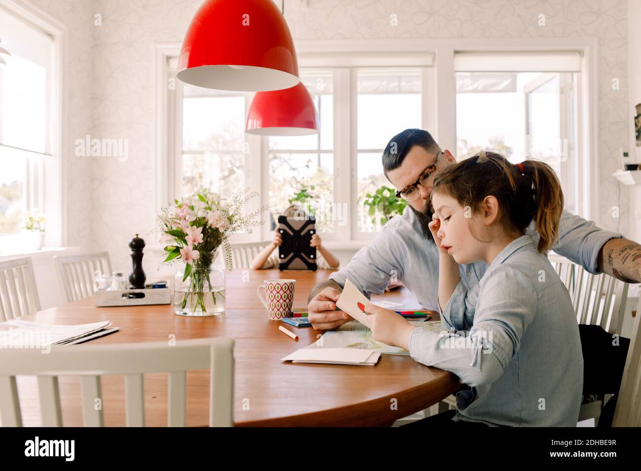 Homme assistant fille tandis que fille utilisant la tablette numérique en arrière-plan à la maison Banque D'Images