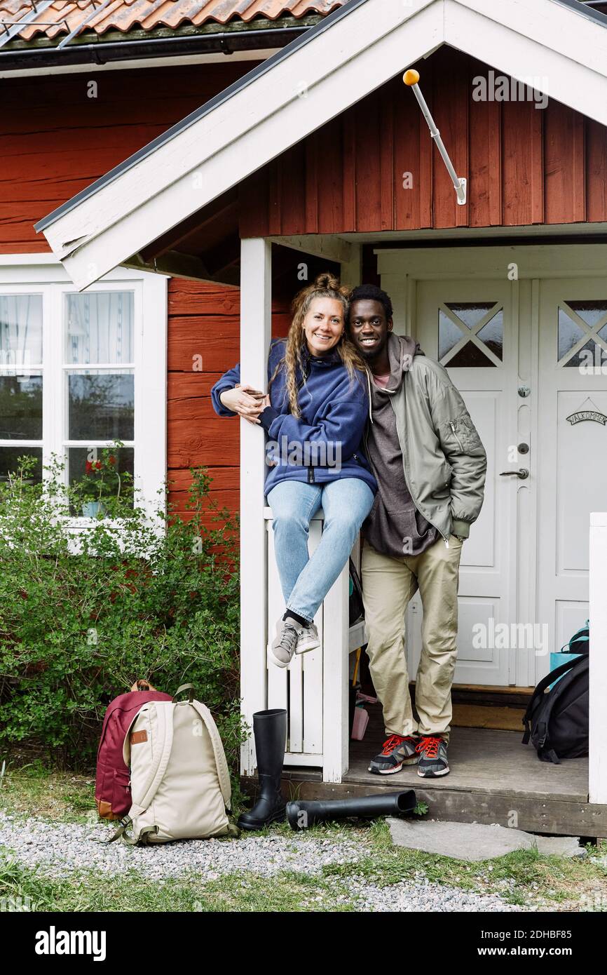 Portrait d'amis souriants avec des sacs à dos à l'entrée du cottage pendant week-end Banque D'Images