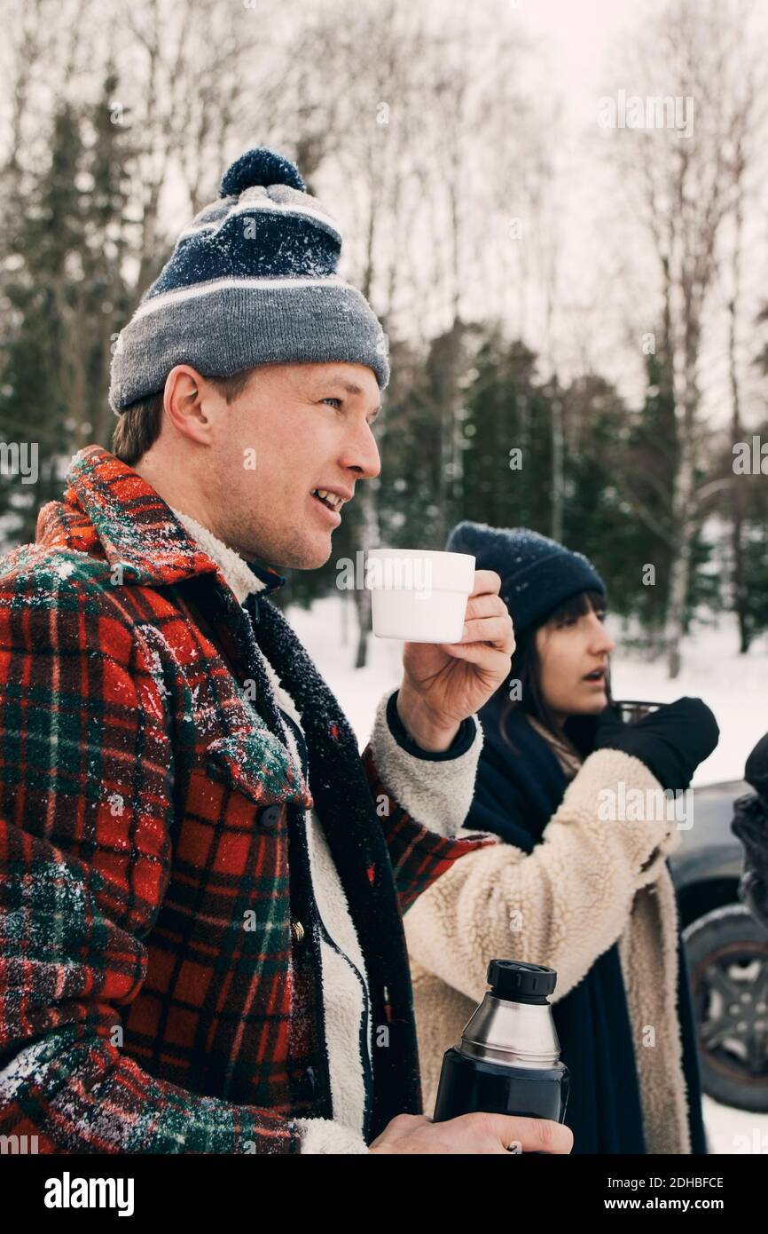 Homme souriant debout avec un ami et prenant un café pendant l'hiver Banque D'Images