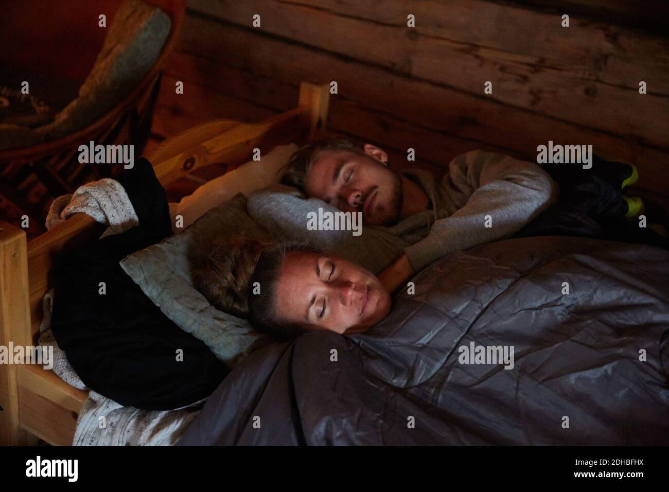 Vue en grand angle d'un couple avec couverture dormant sur le lit dans le cottage Banque D'Images