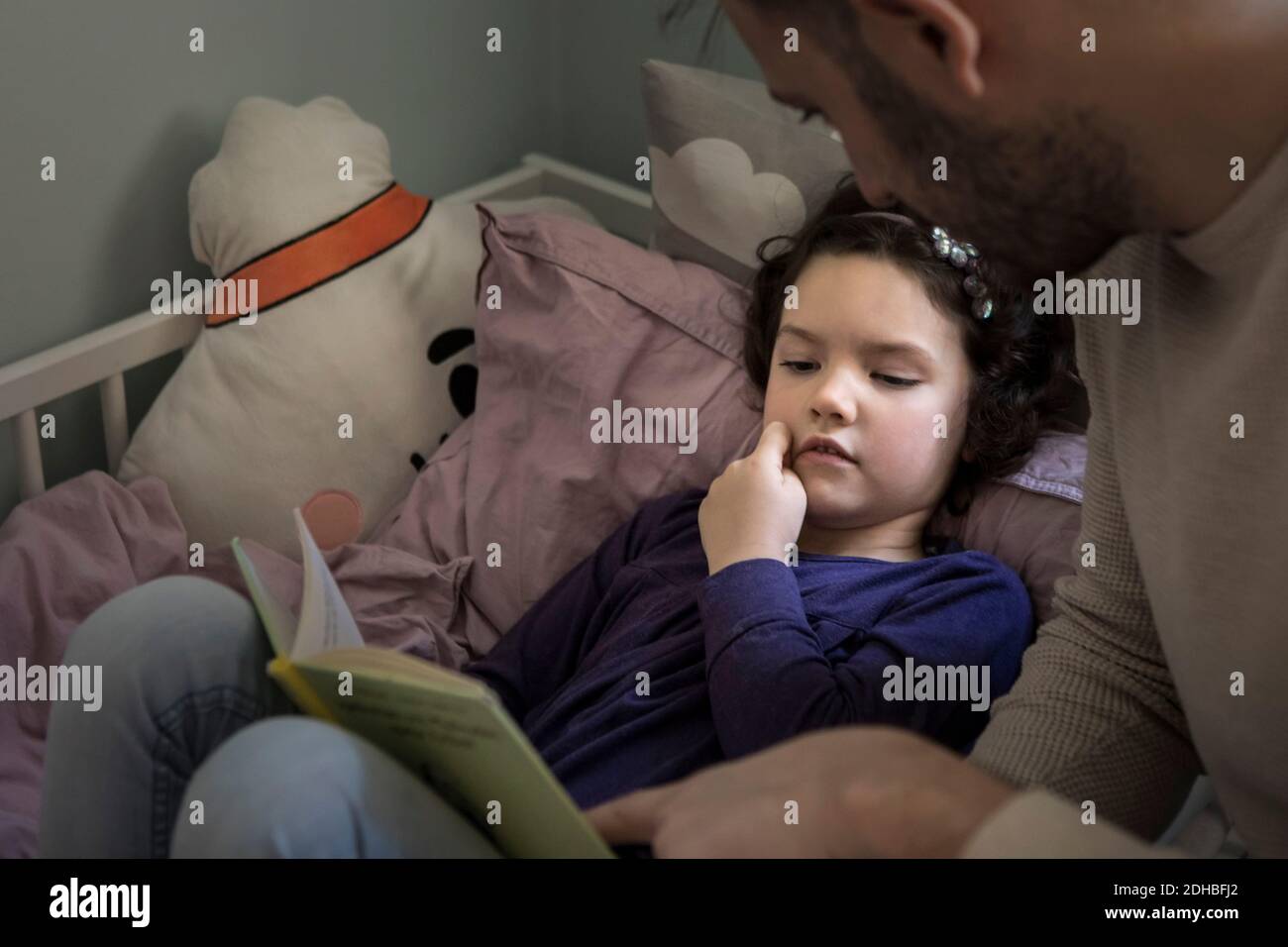 Père racontant l'histoire en lisant un livre à la fille sur le lit à la maison Banque D'Images