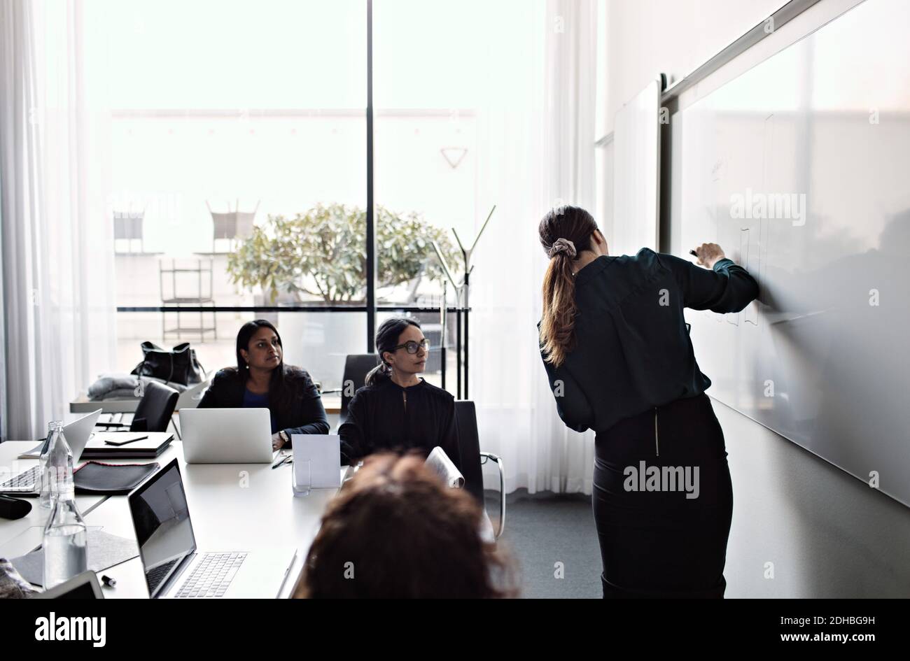 Des collègues féminins se concentrant chez une femme d'affaires expliquant le diagramme sur le tableau blanc pendant réunion dans la salle du conseil Banque D'Images